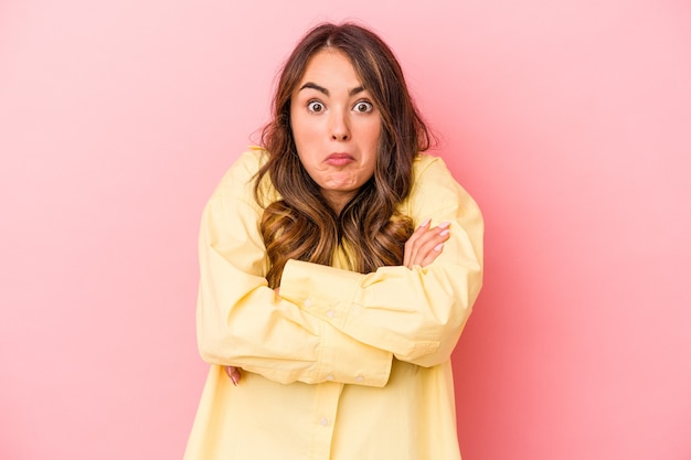 Young caucasian woman isolated on pink background shrugs shoulders and open eyes confused.