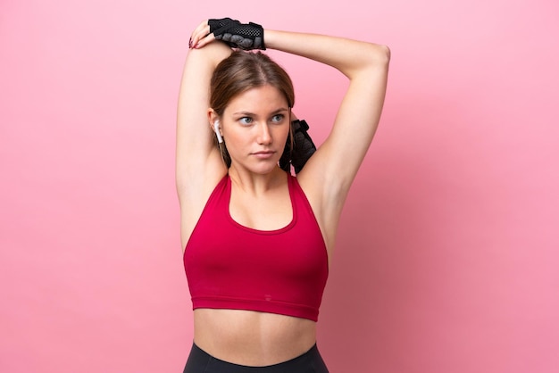 Young caucasian woman isolated on pink background stretching