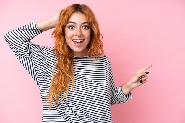 Young caucasian woman isolated on pink background surprised and pointing finger to the side