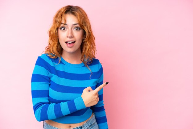 Young caucasian woman isolated on pink background surprised and pointing side