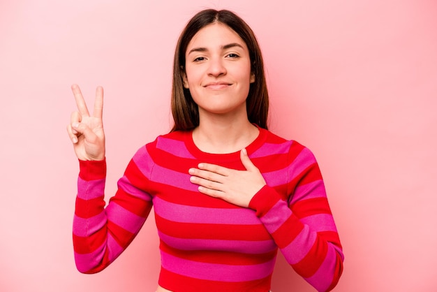 Young caucasian woman isolated on pink background taking an oath putting hand on chest