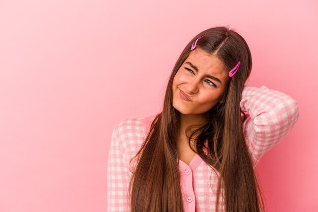 Young caucasian woman isolated on pink background touching back of head, thinking and making a choice.