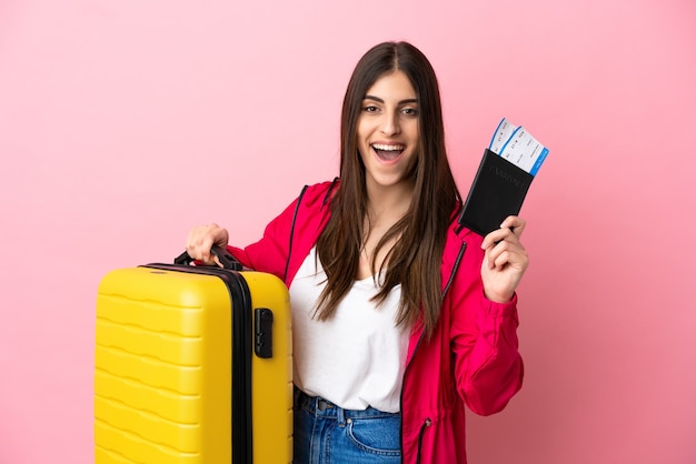 Young caucasian woman isolated on pink background in vacation with suitcase and passport