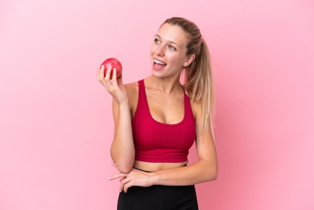 Young caucasian woman isolated on pink background with an apple and happy