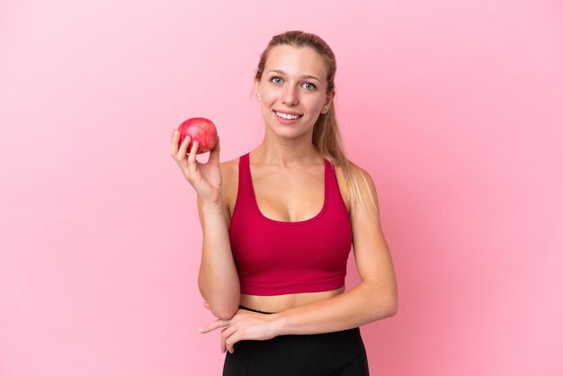 Young caucasian woman isolated on pink background with an apple and happy