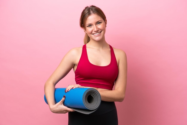 Young caucasian woman isolated on pink background with a mat and smiling