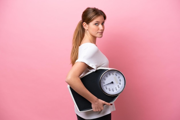 Young caucasian woman isolated on pink background with weighing machine