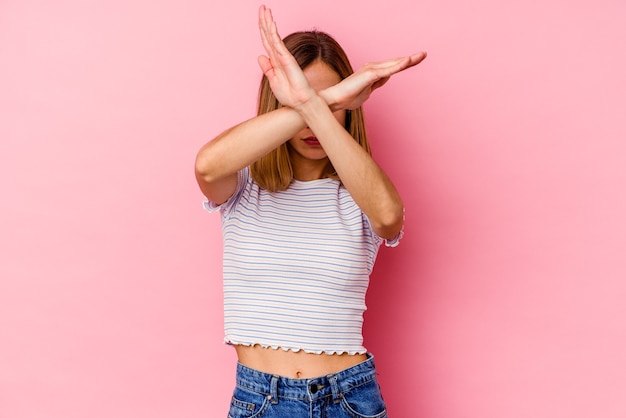 Young caucasian woman isolated on pink keeping two arms crossed, denial concept.