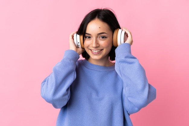 Young caucasian woman isolated on pink listening music