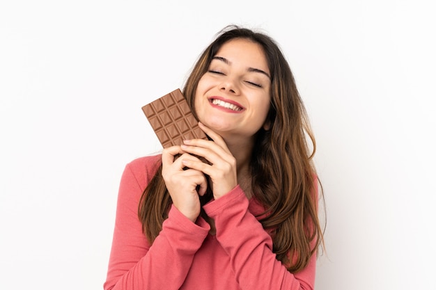 Young caucasian woman isolated on pink taking a chocolate tablet and happy