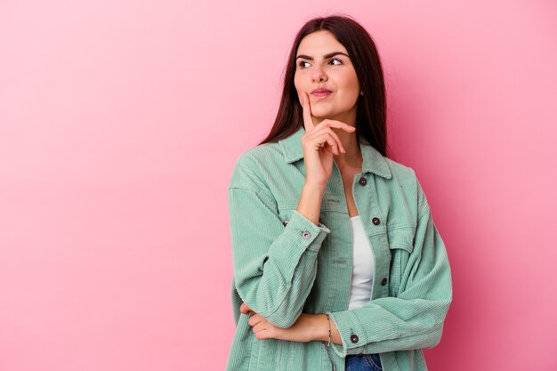 Young caucasian woman isolated on pink wall looking sideways with doubtful and skeptical expression.