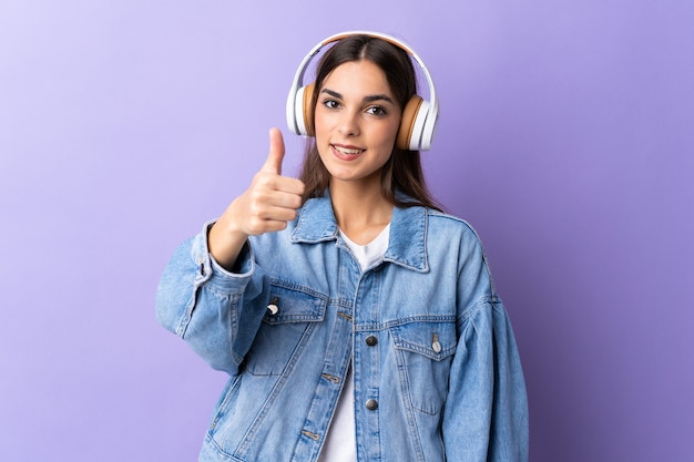 Young caucasian woman isolated on purple background listening music and with thumb up