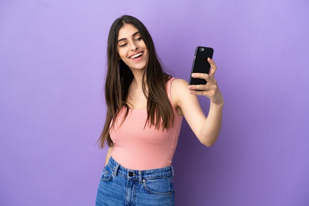 Young caucasian woman isolated on purple background making a selfie