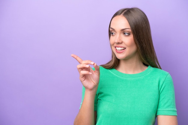 Young caucasian woman isolated on purple background pointing finger to the side and presenting a product