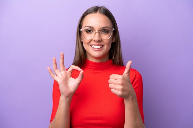 Young caucasian woman isolated on purple background With glasses and doing OK sign