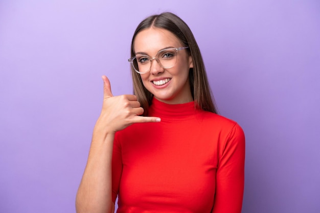 Young caucasian woman isolated on purple background With glasses and doing phone gesture