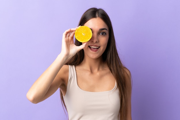 Young caucasian woman isolated on purple holding an orange