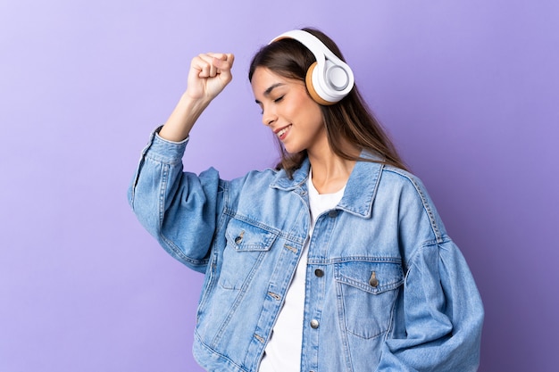 Young caucasian woman isolated on purple listening music and dancing