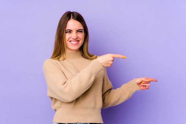 Young caucasian woman isolated on purple pointing with forefingers to a copy space, expressing excitement and desire.