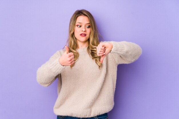 Photo young caucasian woman isolated on purple showing thumbs up and thumbs down, difficult choose concept