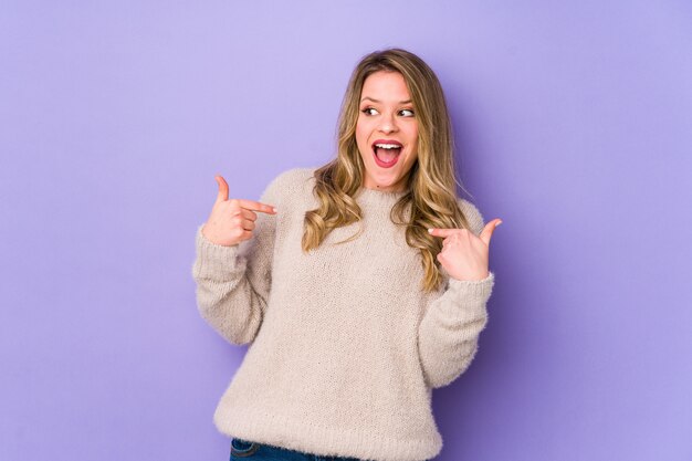 Photo young caucasian woman isolated on purple surprised pointing with finger, smiling broadly.