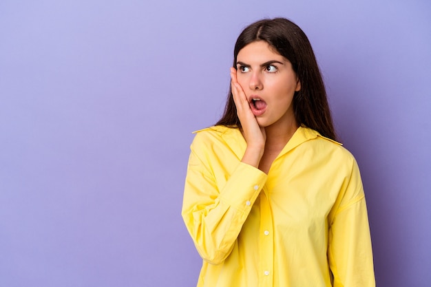 Young caucasian woman isolated on purple wall being shocked because of something she has seen.