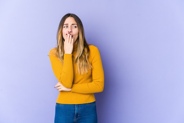 Young caucasian woman isolated on purple wall yawning showing a tired gesture covering mouth with hand.