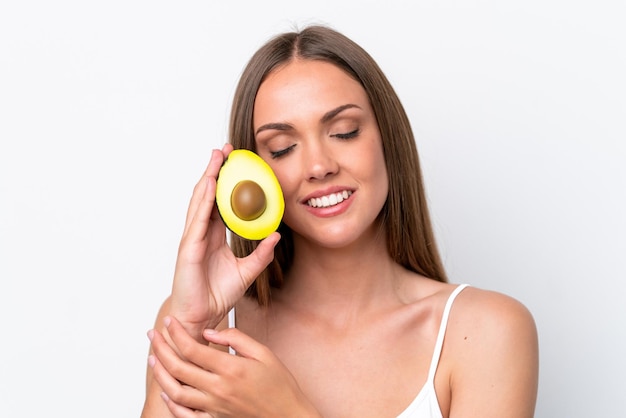 Young caucasian woman isolated on white background holding an avocado while smiling Close up portrait