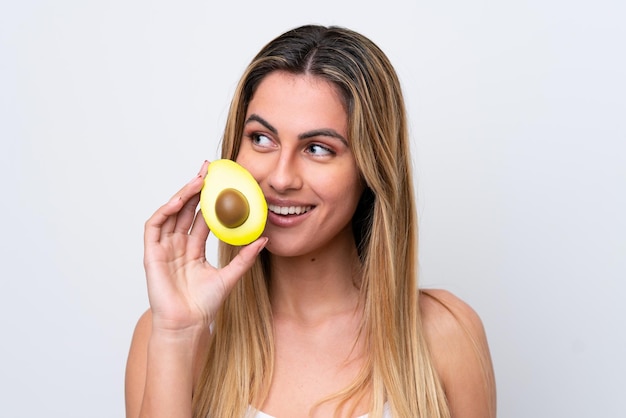 Young caucasian woman isolated on white background holding an avocado while smiling Close up portrait