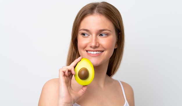 Young caucasian woman isolated on white background holding an avocado while smiling Close up portrait