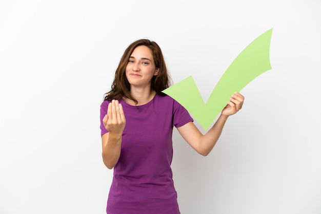 Young caucasian woman isolated on white background holding a check icon and doing coming gesture