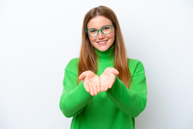 Young caucasian woman isolated on white background holding copyspace imaginary on the palm to insert an ad