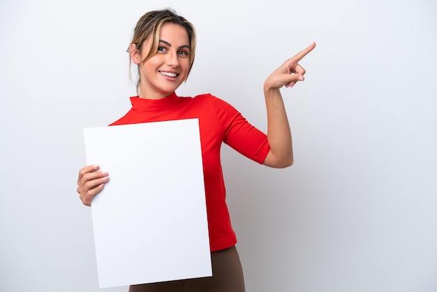 Young caucasian woman isolated on white background holding an empty placard and pointing side