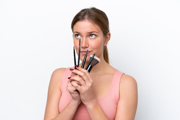 Young caucasian woman isolated on white background holding makeup brush and looking up