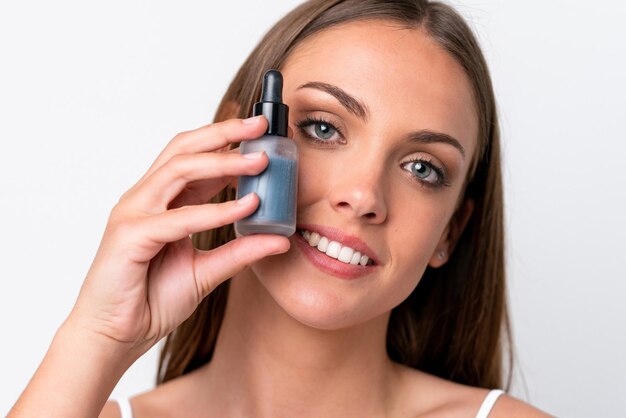 Young caucasian woman isolated on white background holding a serum while smiling Close up portrait