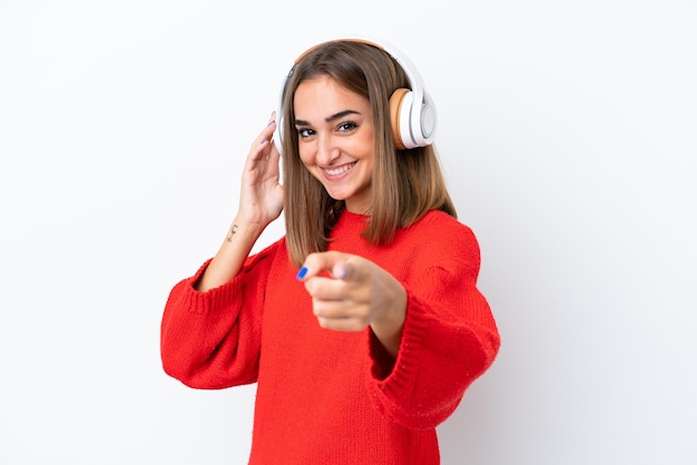 Young caucasian woman isolated on white background listening music and pointing to the front