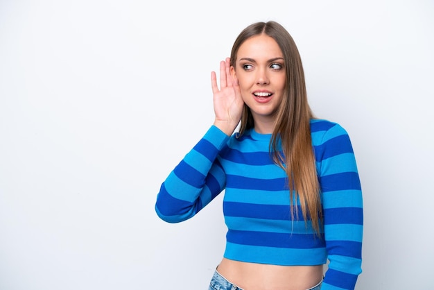 Young caucasian woman isolated on white background listening to something by putting hand on the ear