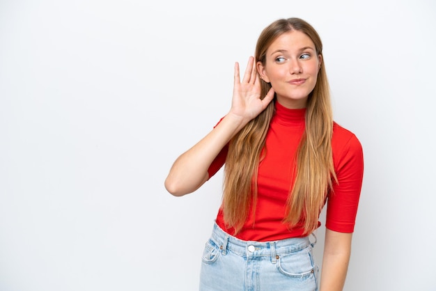 Young caucasian woman isolated on white background listening to something by putting hand on the ear