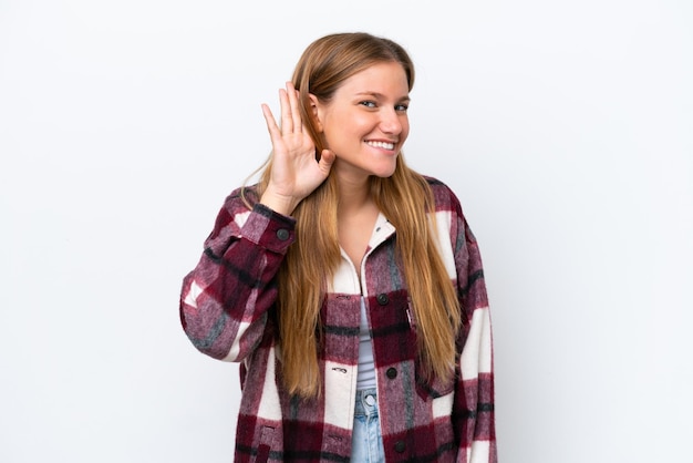 Young caucasian woman isolated on white background listening to something by putting hand on the ear