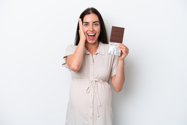 Young caucasian woman isolated on white background pregnant and holding chocolate