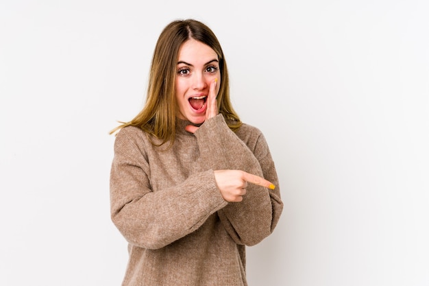 Young caucasian woman isolated on white background saying a gossip, pointing to side reporting something.