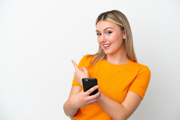 Young caucasian woman isolated on white background using mobile phone and pointing back