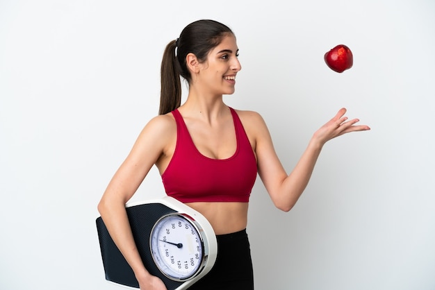 Young caucasian woman isolated on white background with weighing machine and with an apple