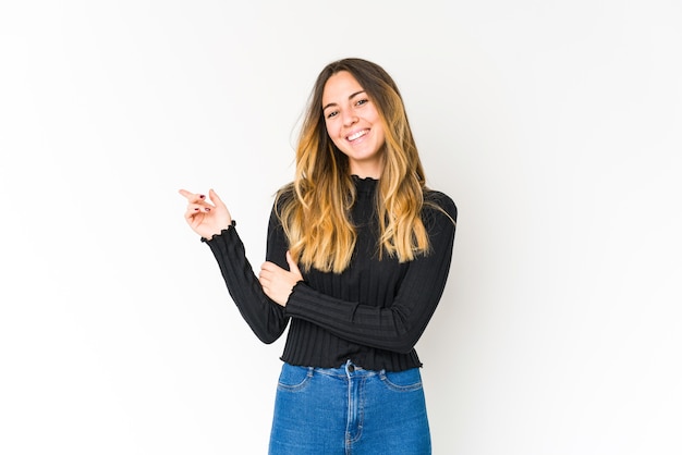 Young caucasian woman isolated on white space smiling cheerfully pointing with forefinger away.