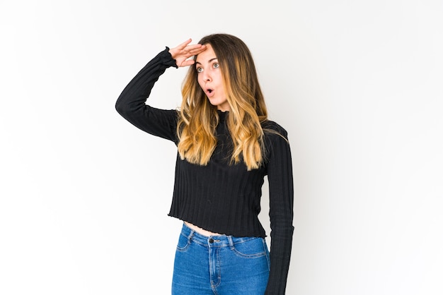 Young caucasian woman isolated on white wall looking far away keeping hand on forehead.