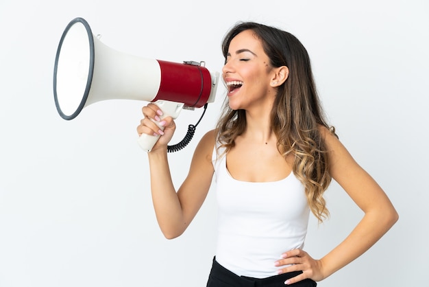 Young caucasian woman isolated on white wall shouting through a megaphone to announce something in lateral position