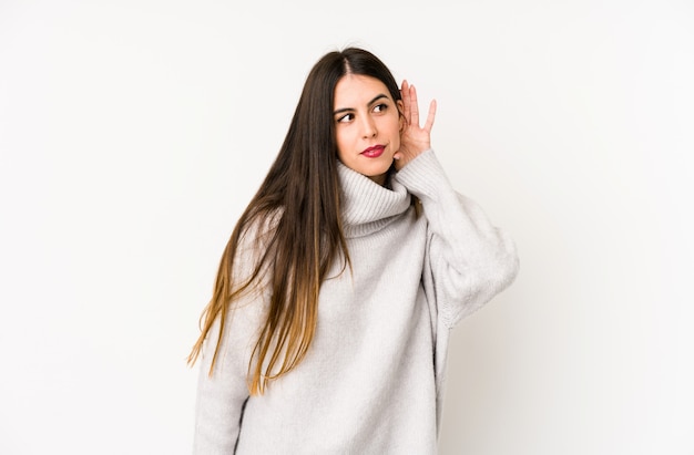 Young caucasian woman isolated on a white wall trying to listening a gossip.