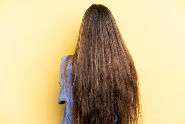 Young caucasian woman isolated on yellow background in back position