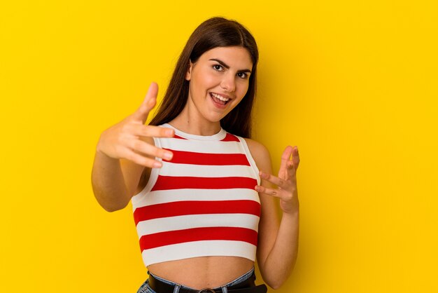 Young caucasian woman isolated on yellow background feels confident giving a hug to the camera.