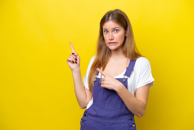 Young caucasian woman isolated on yellow background frightened and pointing to the side